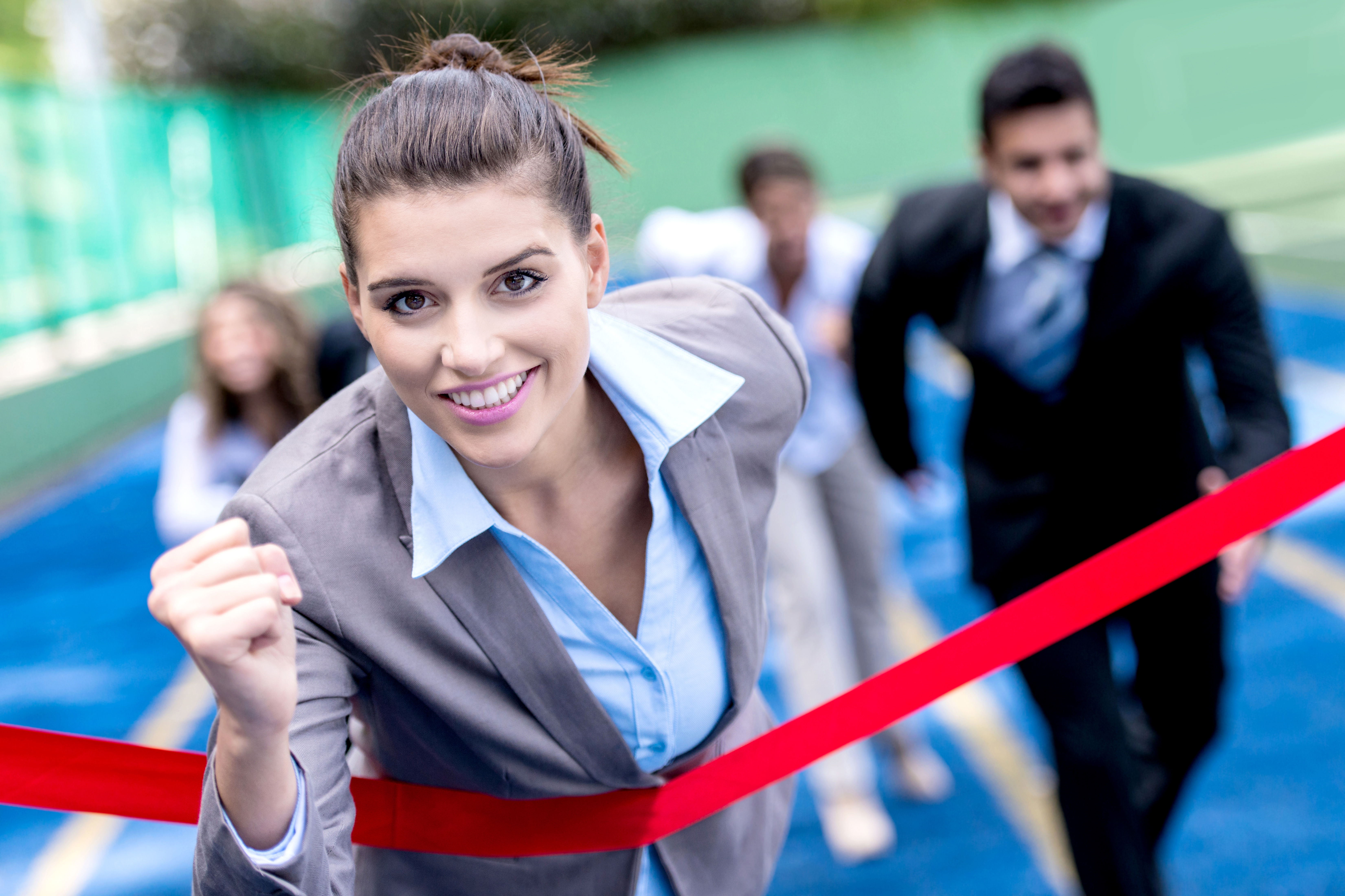 Stock image of a group of people in business suits racing on a race track. A woman is crossing the finish line. 